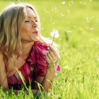 girl blowing on a dandelion lying on the grass