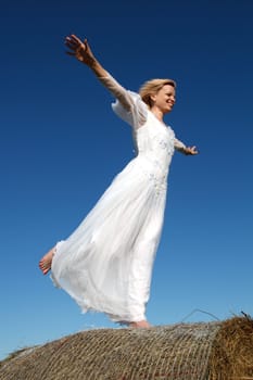 Young woman standing on a straw bale against a blue sky