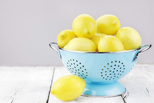 Blue colander filled with fresh lemons over a rustic background.
