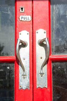 A red painted wooden door with a pair of metal retro doorhandles and a pull sign and keyhole.