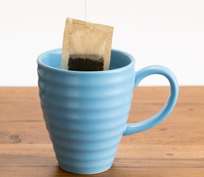 Organic green tea or herbal tea being lowered into a blue mug on wooden table