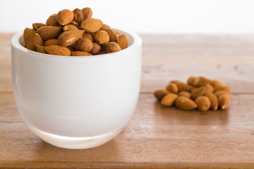 Raw almond nuts in white glass bowl on old wooden table