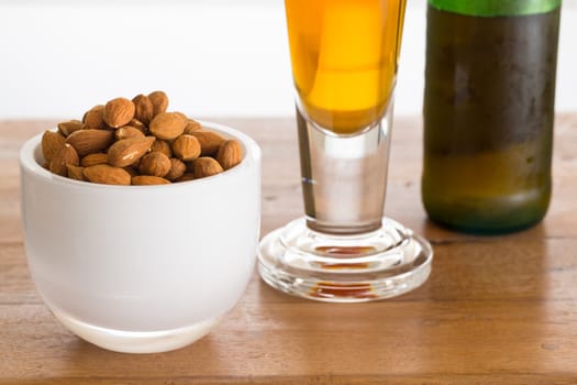 Raw almond nuts in white glass bowl on old wooden table with glass of cold beer