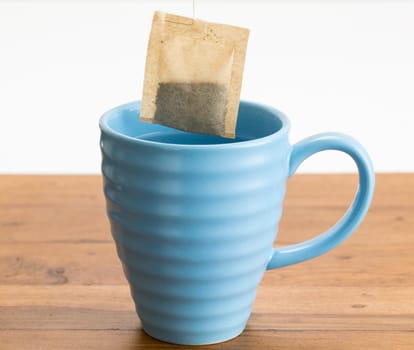 Organic green tea or herbal tea being lowered into a blue mug on wooden table