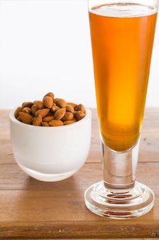 Raw almond nuts in white glass bowl on old wooden table with glass of cold beer