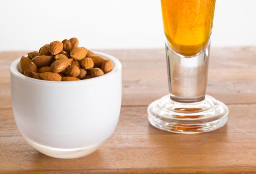 Raw almond nuts in white glass bowl on old wooden table with glass of cold beer