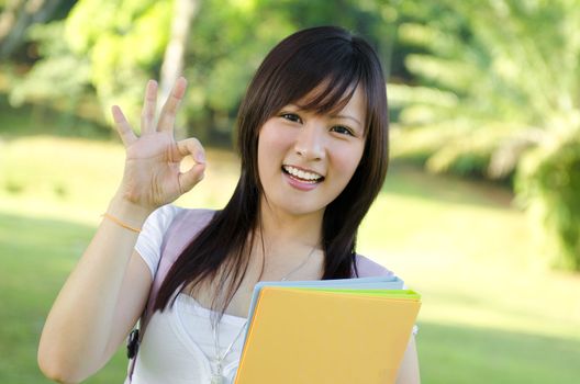 Cheerful Asian university student giving an okay hand sign