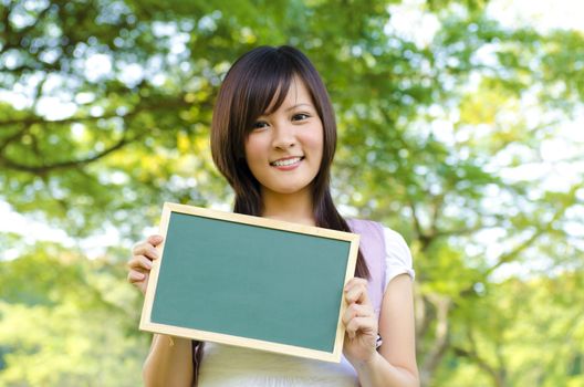 Young Asian college girl holding a blackboard outdoor, green park