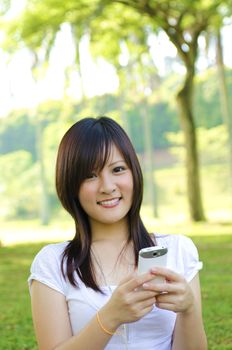 Happy oriental Asian young student using mobile phone to online / texting / sms , outdoor green park