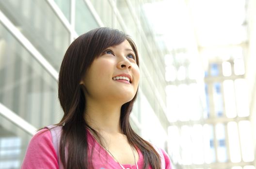 A young Asian girl looking far away to bright light in front of a modern building.