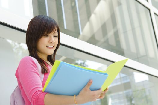 Asian teen student reading file folder outside school building