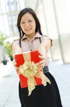 Young Asian girl arms out holding a beautiful wrapped present. Focus is on the ribbons.