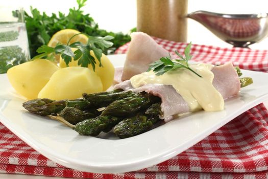 Asparagus with hollandaise sauce, cooked ham and potatoes on a light background
