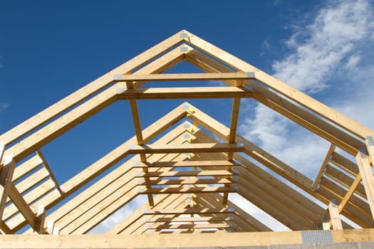 A new build roof with a wooden truss framework making an apex against a blue sky with cloud.