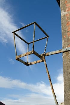 A vintage metal brazier with paint and rust fixed to a brick wall with a metal bracket against a blue sky with cloud.