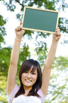 Young Asian college girl arms up holding a blackboard outdoor, green park
