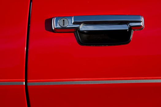A vintage car door handle made of metal with pull up lever and keyhole on a red door with stripe.