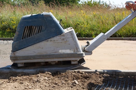Brick paver build new sidewalk. worker with rammer press sand before the brick laying
