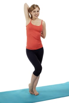 young happy fitness woman standing on a blue mat stretching her arms on white background