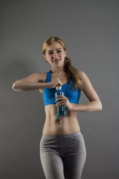young fitness woman opening a bottle with water on grey background