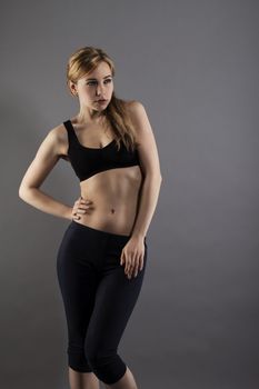 young fitness woman in fashion pose on grey background