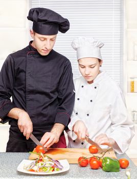 Senior chef teaches young chef to properly cut vegetables