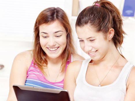 Two happy teenage girls using tablet computer at home