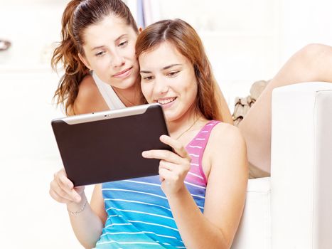 Two happy teenage girls using tablet computer at home