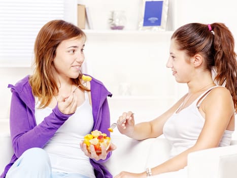 Teenage girls chatting and eating fruit salad at home