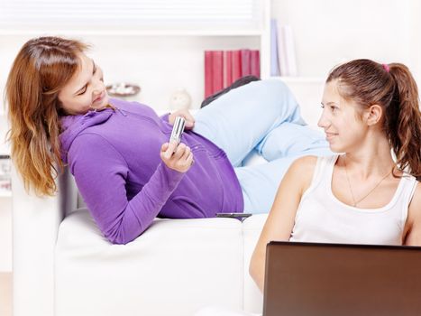 Two happy teenage girls having fun using electronic gadgets at home