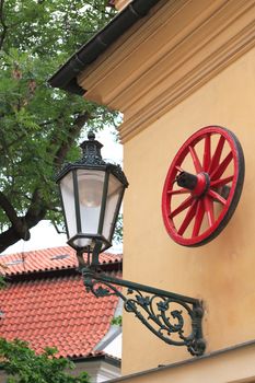 Stylish vintage lantern and red cart wheel on building wall