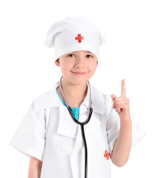Portrait of a smiling little girl wearing as a doctor on white uniform, with a stethoscope, while pointing finger up and gives instructions. Isolated on white background.