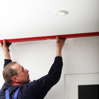 A middle-aged man uses a red spirit level to test that the ceiling is horizontal