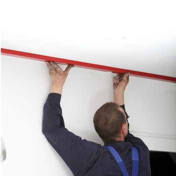 Man using a large red spirit level on the ceiling in a DIY home maintenance concept