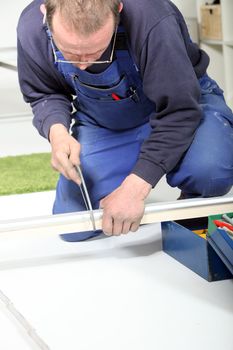 Middle-aged man kneeling on the ground exerting force on a power drill being used to drill a metal track.