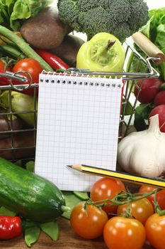 Basket with fresh vegetables and shopping list and pencil on a wooden background