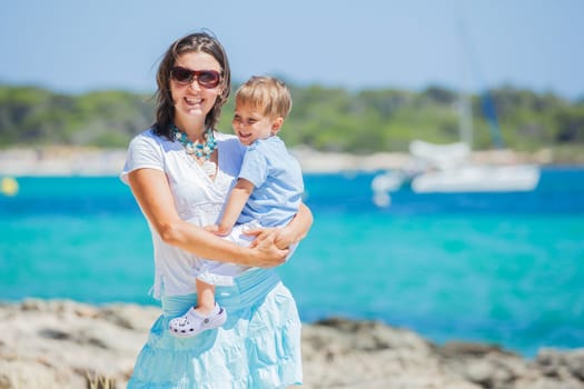 Young beautiful woman wis her son walking along tropical beach
