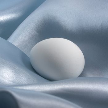 noble easter theme showing a white egg in blue satin fabrics