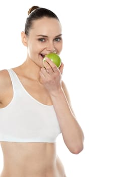 Pretty fit trendy woman eating fresh green apple isolated over white