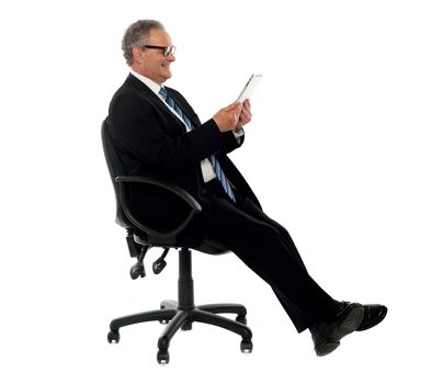 Well dressed corporate male holding wireless tablet, seated on chair, side pose