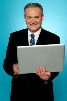 Smiling aged executive holding laptop and looking at camera