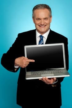 Aged corporate male pointing at laptop screen isolated over gradient background