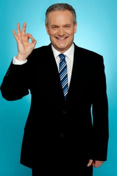 Handsome portrait of experienced businessman showing okay sign over gradient background