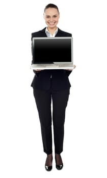 Full length portrait of attractive smiling woman presenting new laptop to you
