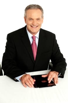 Portrait of happy aged businessman sitting with tablet on desk against white background