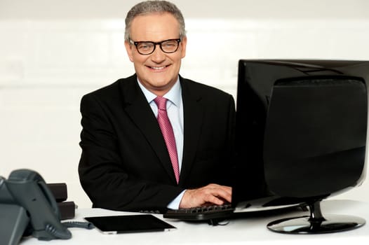 Happy aged corporate man typing on keyboard while looking at you