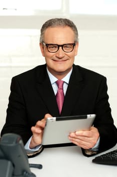 Senior executive sitting with tablet pc in hands and smiling at camera