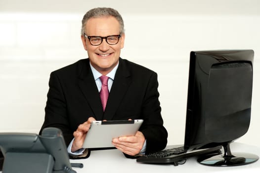 Aged businessman in glasses using tablet sitting in office