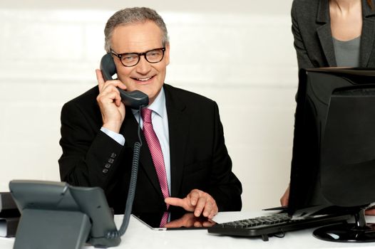 Aged businessman communicating on phone with secretary standing beside