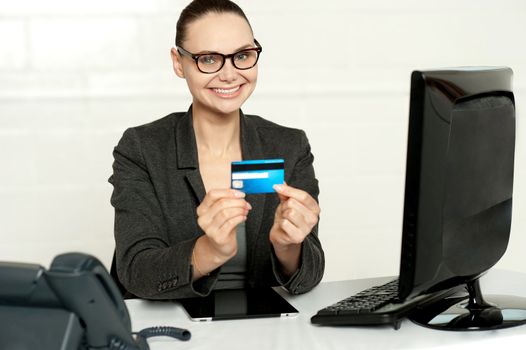 Smiling corporate lady in her office showing credit card to camera
